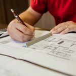 Architect working on floor plans with ruler and pencil in an office setting.